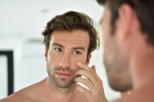 man touching his face while looking in mirror