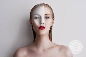 Blond woman wearing red lipstick and white face paint in front of a white backdrop