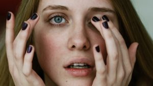 close up of dark haired woman with green eyes and black nail polish rubbing her eyes