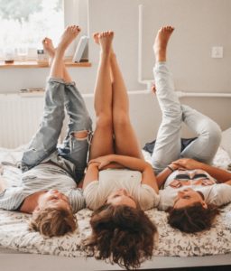 3 girls laying on their backs in bed with feet up