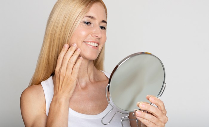 Blonde woman smiling and touching her cheek looking in the mirror
