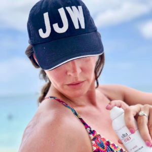 Woman at the beach wearing "JJW" hat applying sunscreen
