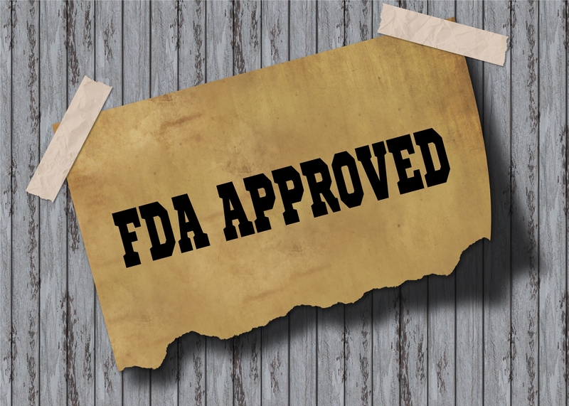 Yellow paper reading "FDA Approved" in black letters taped to a piece of grey wood