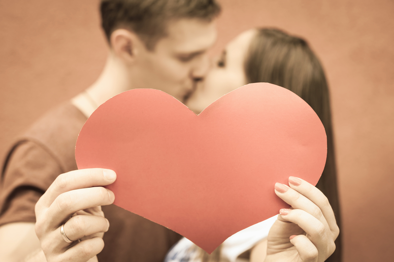 young caucasian man and woman kissing and holding up a red heart