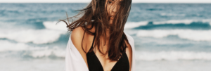 Young brunette woman wearing a black bikini top and white coverup in front of the ocean