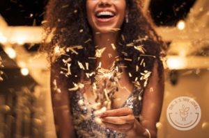 smiling african american woman in gold dress holding a gold sparkler