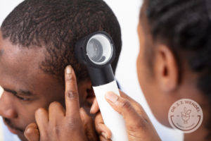 Doctor examing young black man's hair with dermatoscopy