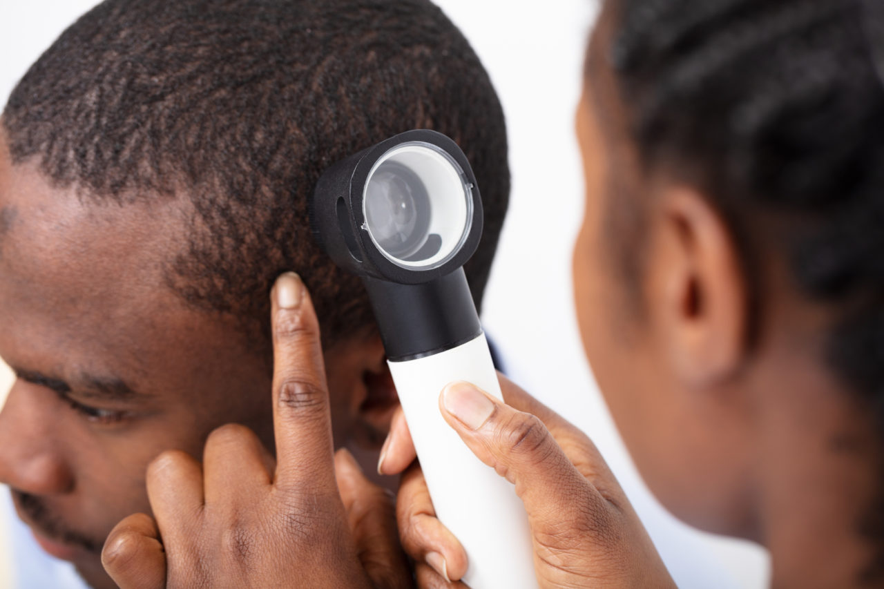 Doctor examing young black man's hair with dermatoscopy