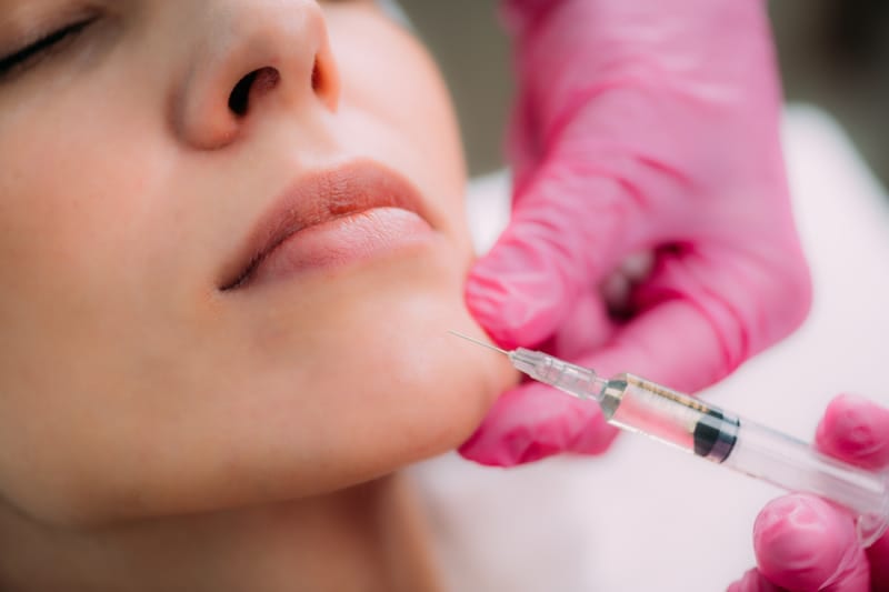 woman recieving chin filler by provider with pink gloves