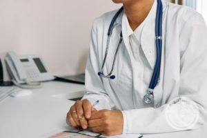 Healthcare worker wearing stethoscope sitting at desk taking notes