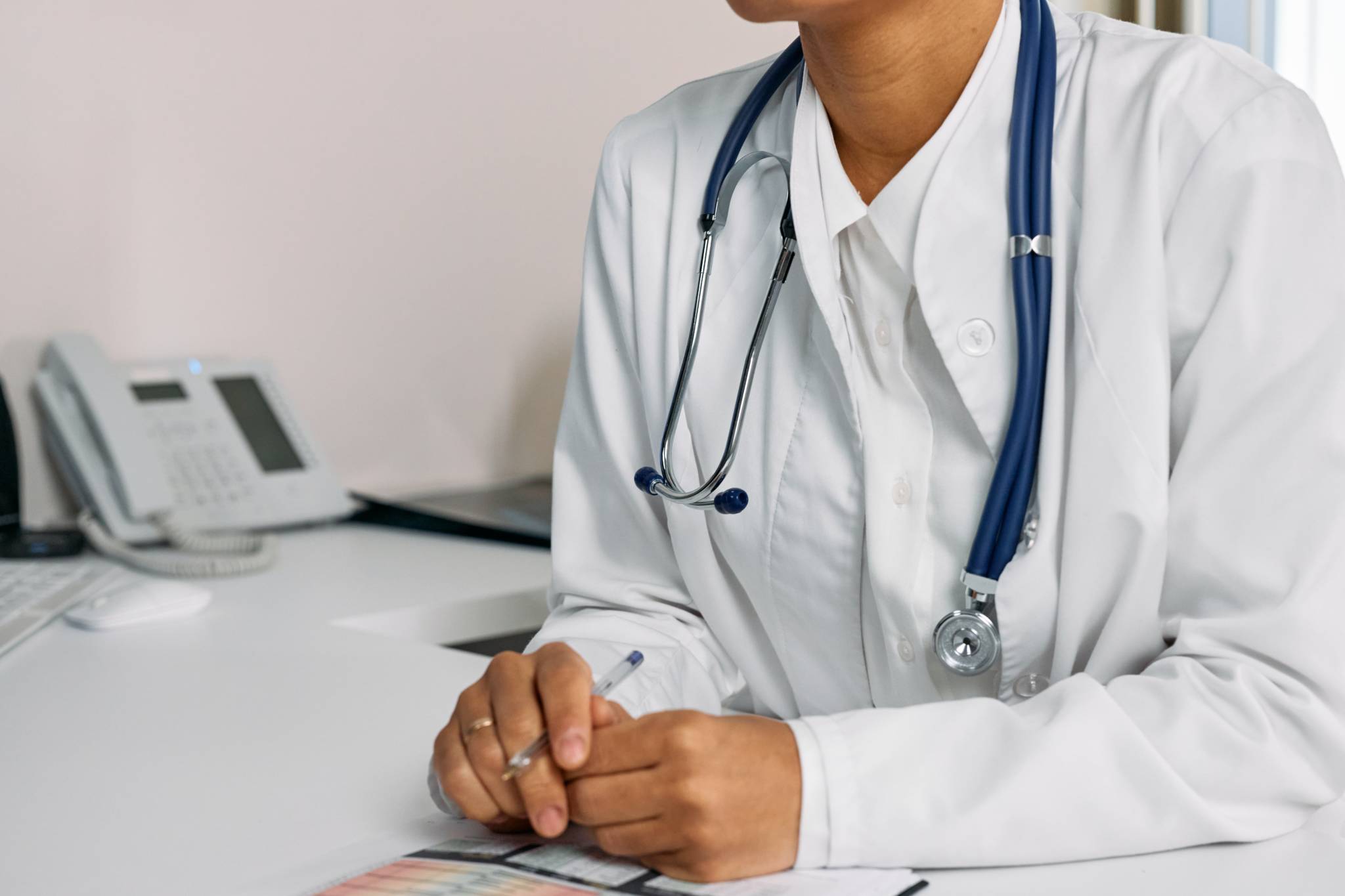 Healthcare worker wearing stethoscope sitting at desk taking notes