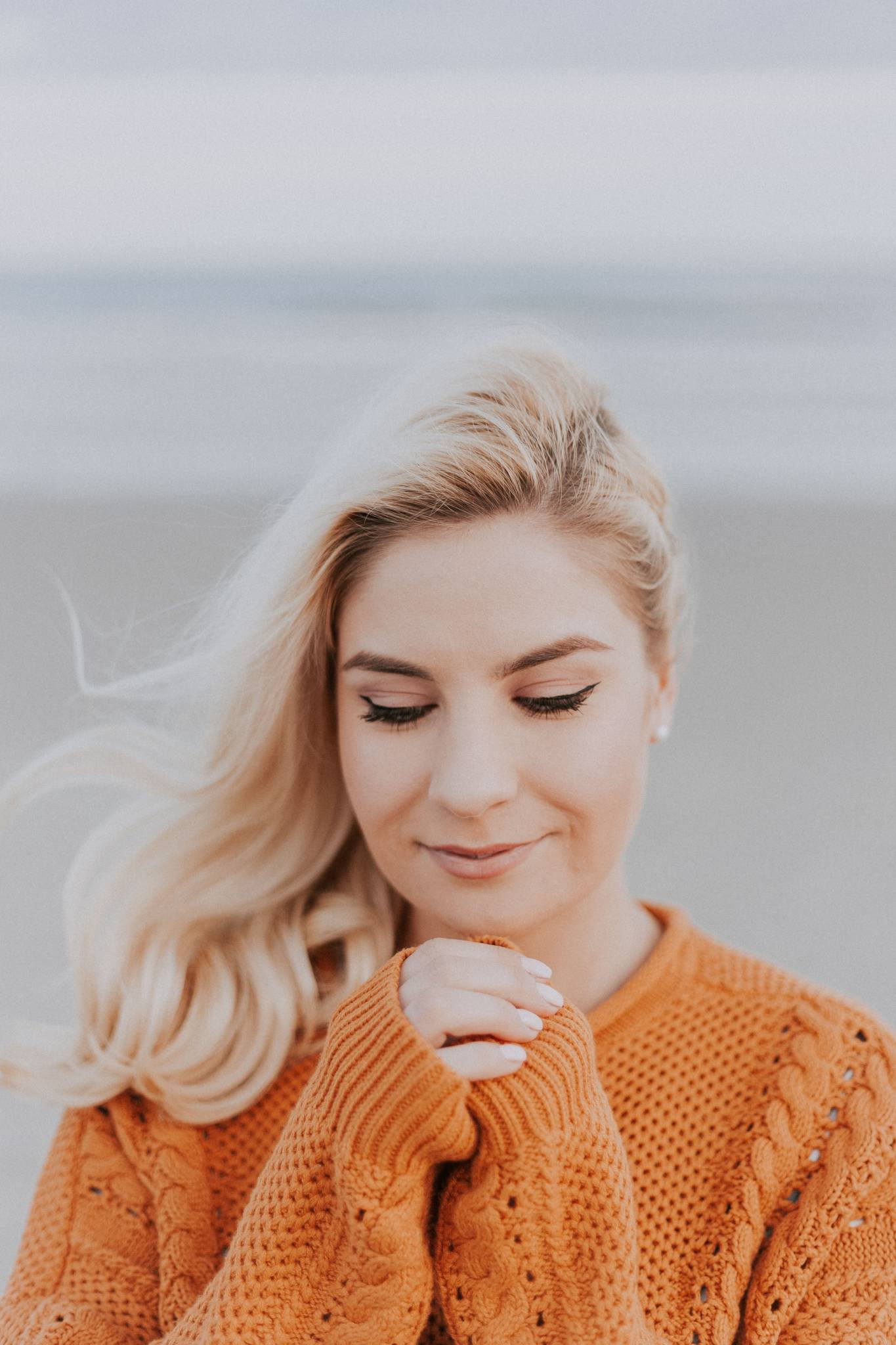 Blonde woman wearing orange sweater standing outside