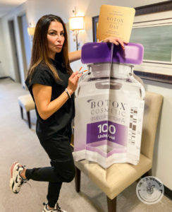 lori lankford with cardboard botox bottle sign for national botox day 2021
