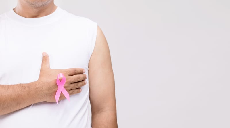 man holding hand to chest with pink breast cancer ribbon