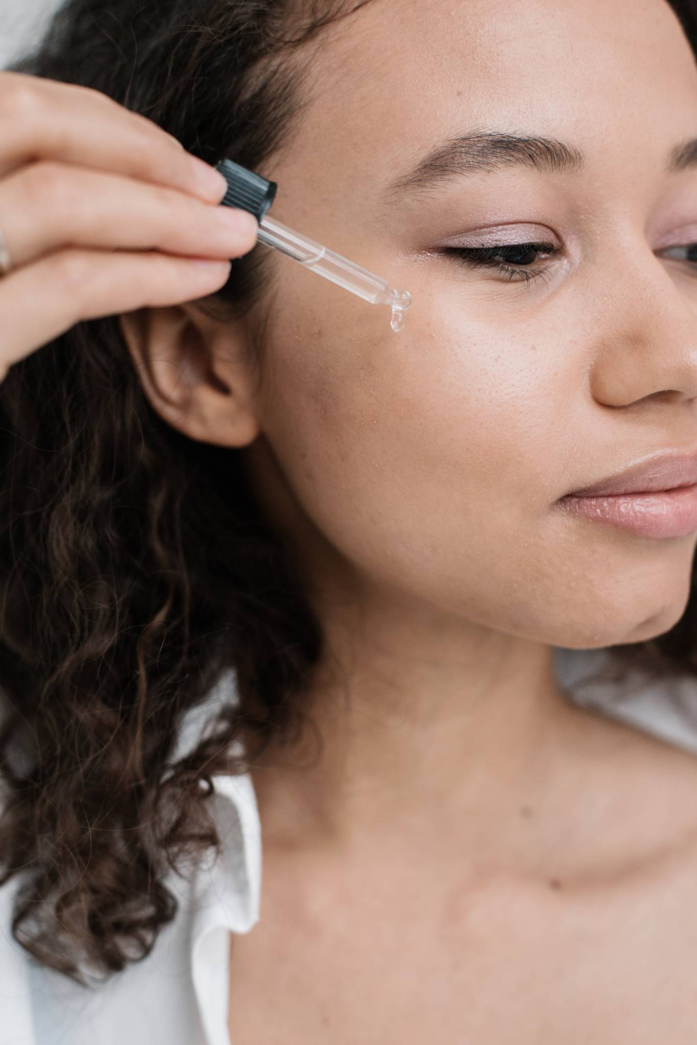 dark skinned woman using applicator to apply oil to face