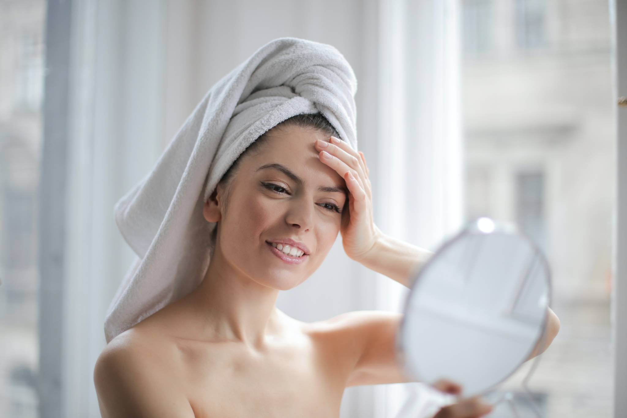 woman wearing a towel on head looking into makeup mirror