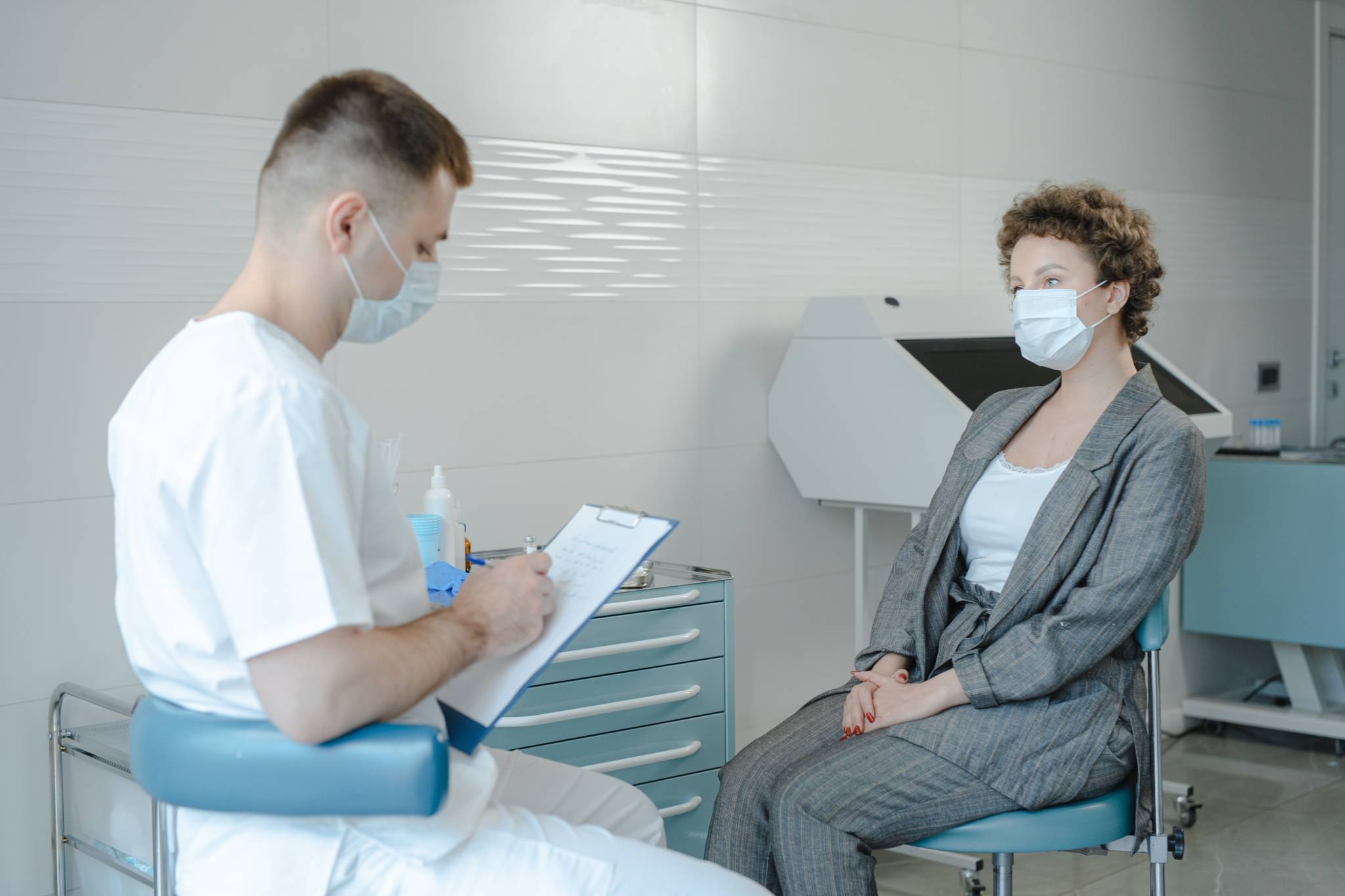 male doctor writing on notepad while speaking to female patient. both are wearing masks
