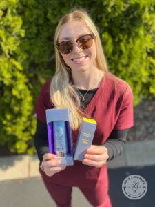 dr j j wendel employee holding up skinmedica sunscreen products while wearing scrubs outside in front of a hedge