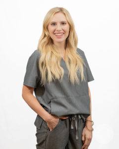 female nurse in gray scrubs smiling with hand in pocket