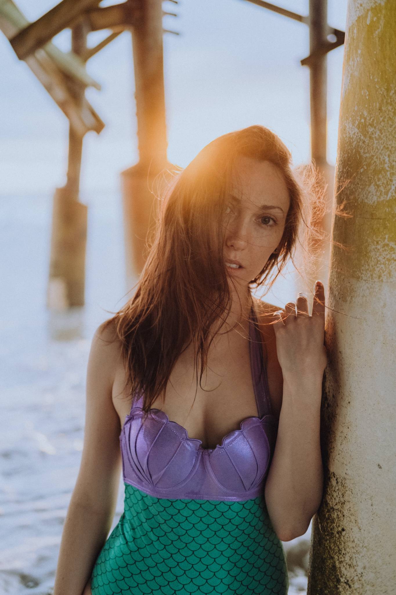 woman standing under boardwalk wearing one piece swimsuit with purple top and green bottom