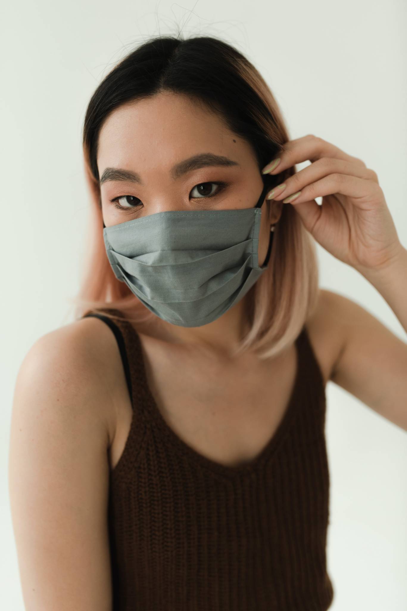 asian woman in maroon tank top wearing mask and touching side of face