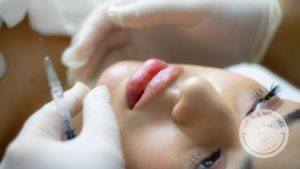 womans face laying down and person with white gloves injecting dermal filler in face