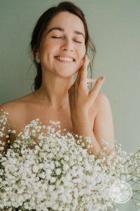 woman hiding body behind white flowers smiling and touching cheek with her hand