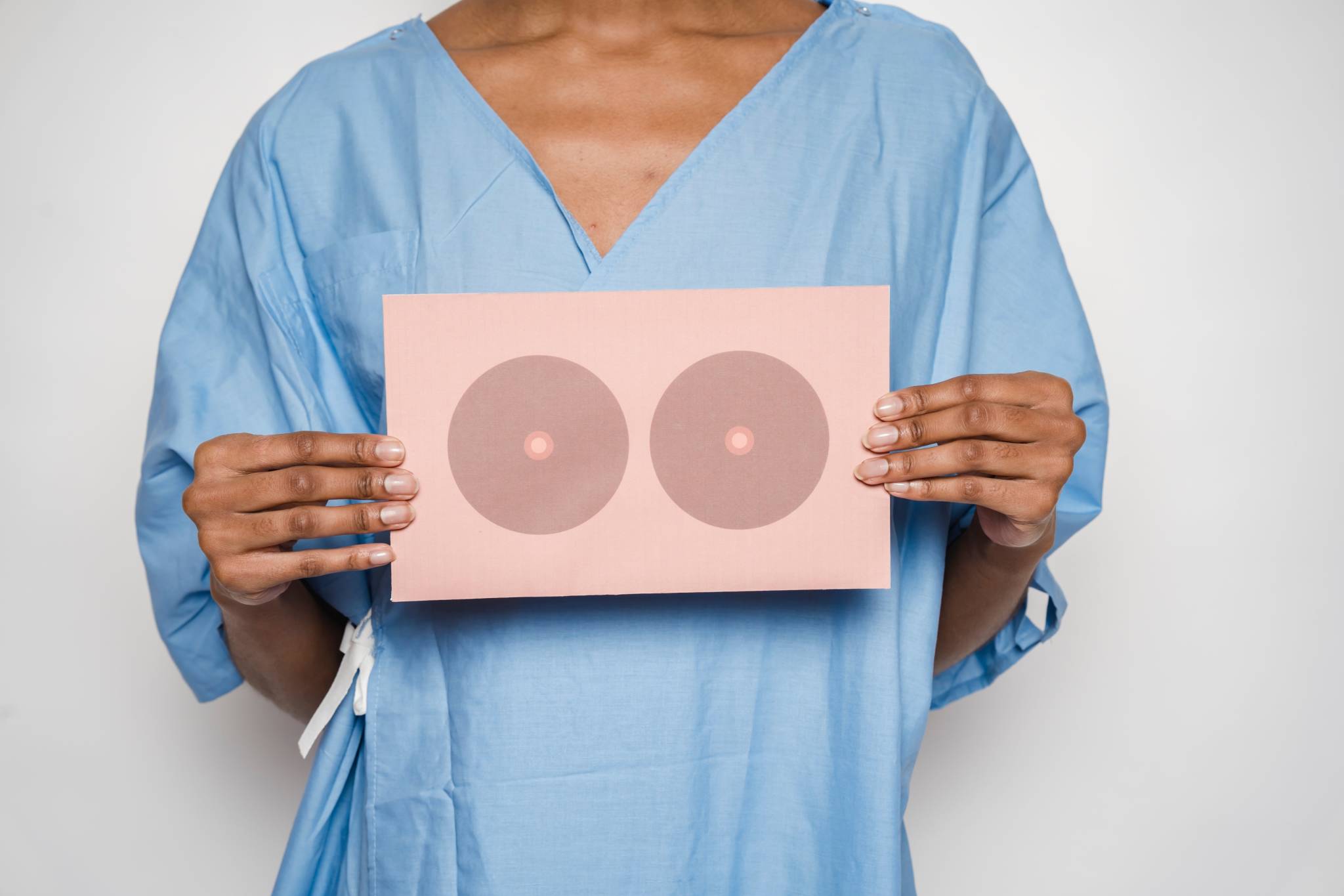 woman wearing light blue medical gown and holding pink card with a drawing of breasts on the front