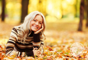 woman in striped brown sweater smiling and laying in orange leaves