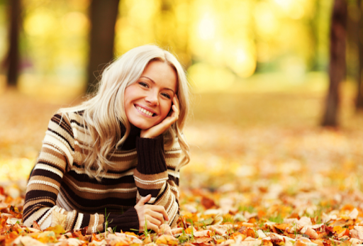 woman in striped brown sweater smiling and laying in orange leaves