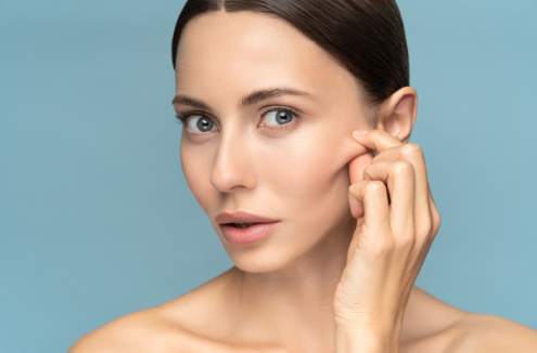 woman with brown hair in front of blue background pinches face on cheek