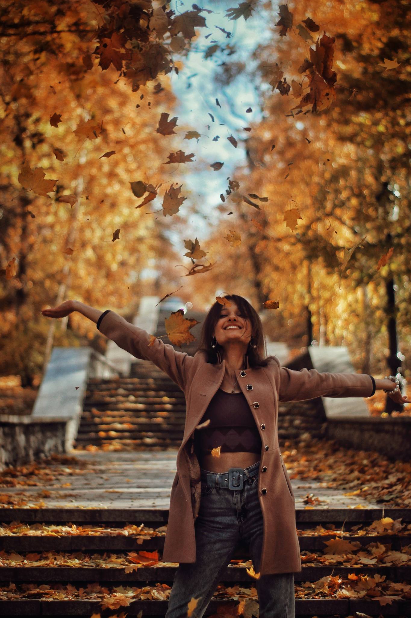 woman outside on steps smiling and looking up as leaves fall from trees