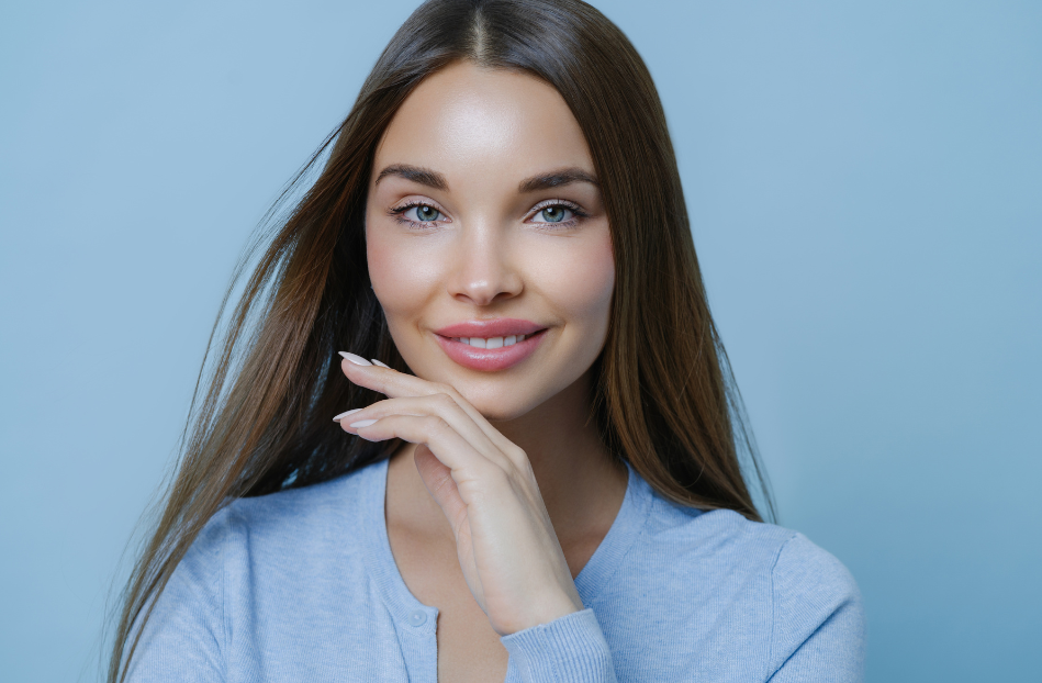 brunette woman wearing blue sweater smiles and touches jawline