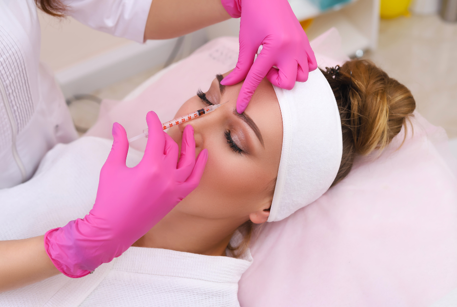 Woman wearing pink gloves injects cosmetic injectable in women's frown lines