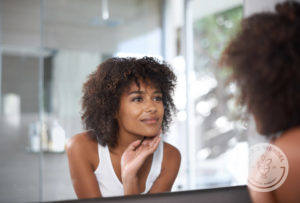 young black woman gazes at herself in bathroom mirror