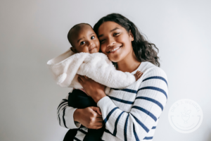 woman of color holds her baby while smiling