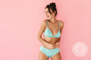 fit woman wearing mint colored undergarments in front of a pink background