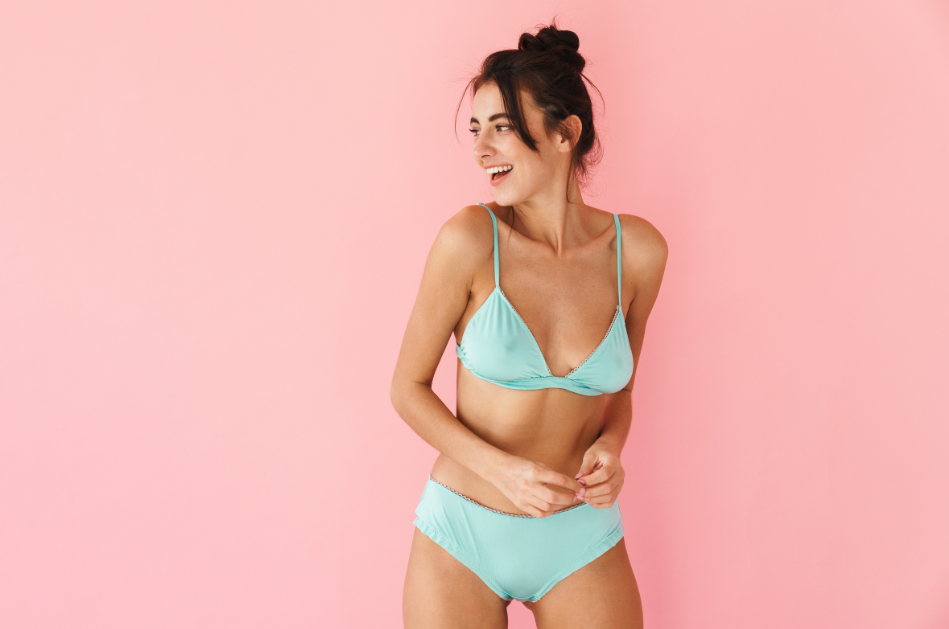 fit woman wearing mint colored undergarments in front of a pink background