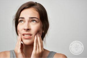 brunette woman holds jaw in her hands in pain