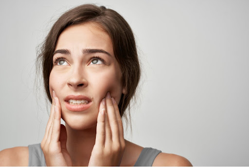 brunette woman holds jaw in her hands in pain