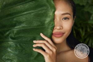 Young woman peeking from behind large green leaf