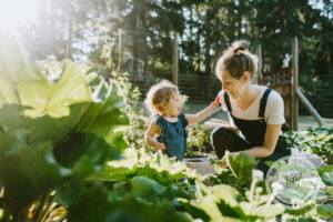 Blonde mother and child in green garden picking strawberries