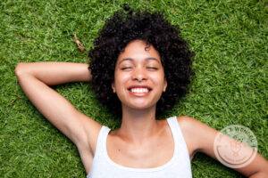 Woman with curly hair laying on bed of grass and smiling