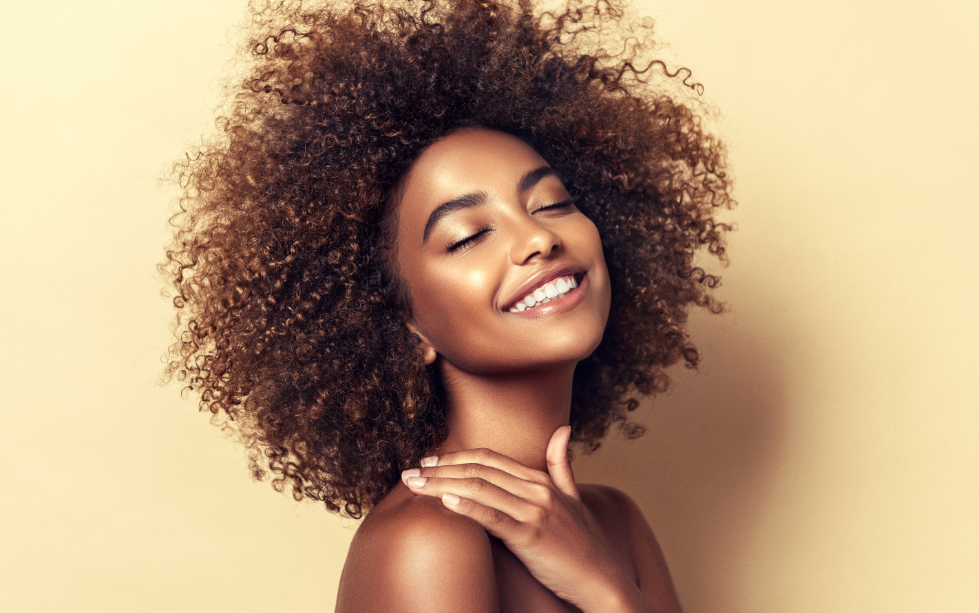black woman with curly hair smiling with her eyes closed and her hand placed on her shoulder