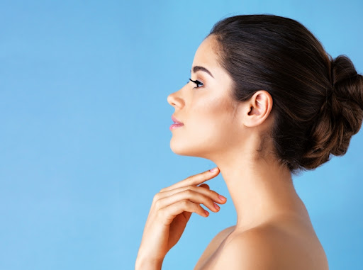side profile of woman touching her neck against a blue background
