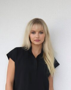 blonde woman looking at camera in black shirt against white background