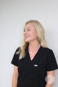 blonde certified aesthetic laser operator woman smiling in black scrubs