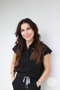 brunette woman smiling at camera in black uniform against white wall