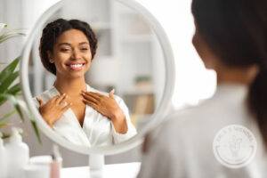 woman wearing robe smiling and looking at her reflection in the mirror