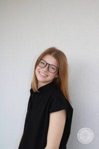 Woman in glasses with head turned and smiling at camera